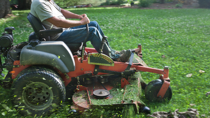 Foto de una persona cortando su césped con un tractor cortacésped