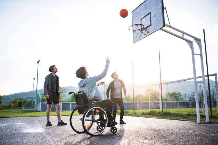 A young man in a wheelchair plays basketball with his two friends on a court.