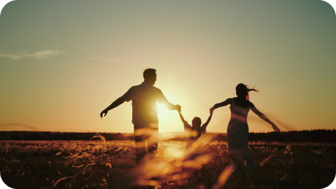 Parents playing with young child in a field at sunset.