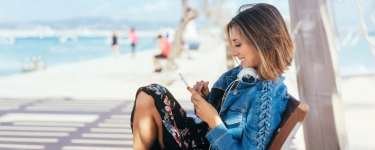 Foto de mujer en la playa usando su teléfono con el logo de Zelle