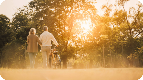 Two older people walk in a field with a bike.
